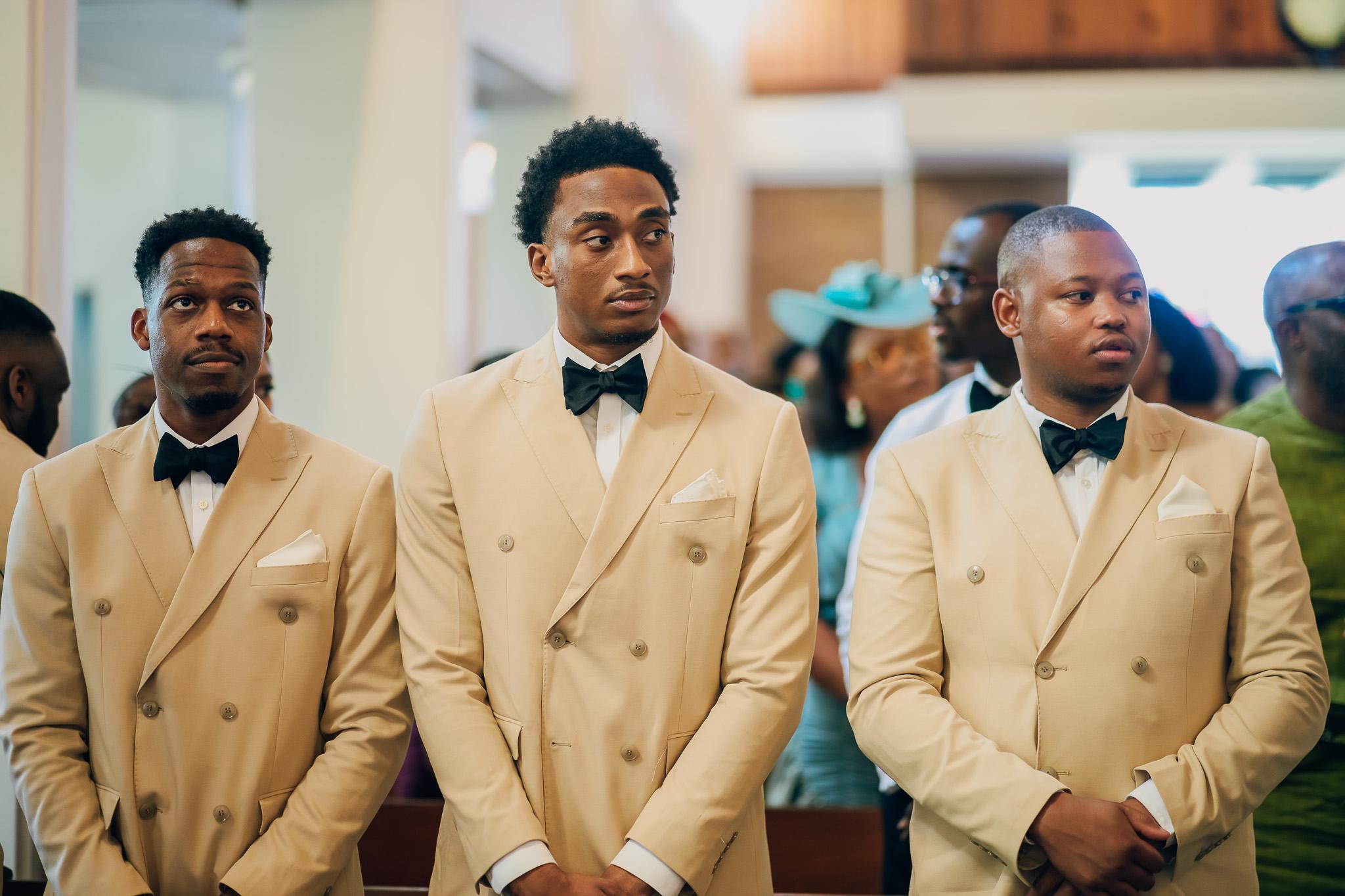 Three groomsmen in cream jackets standing together in church.