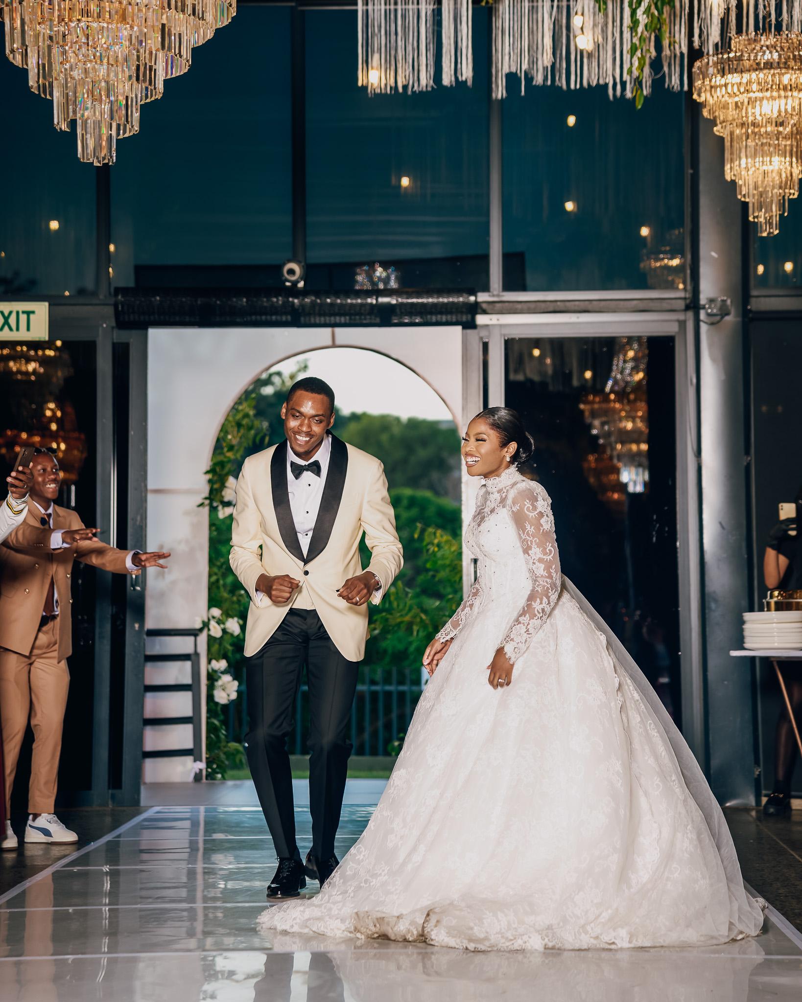 Bride and groom celebrating beneath chandeliers at their reception.