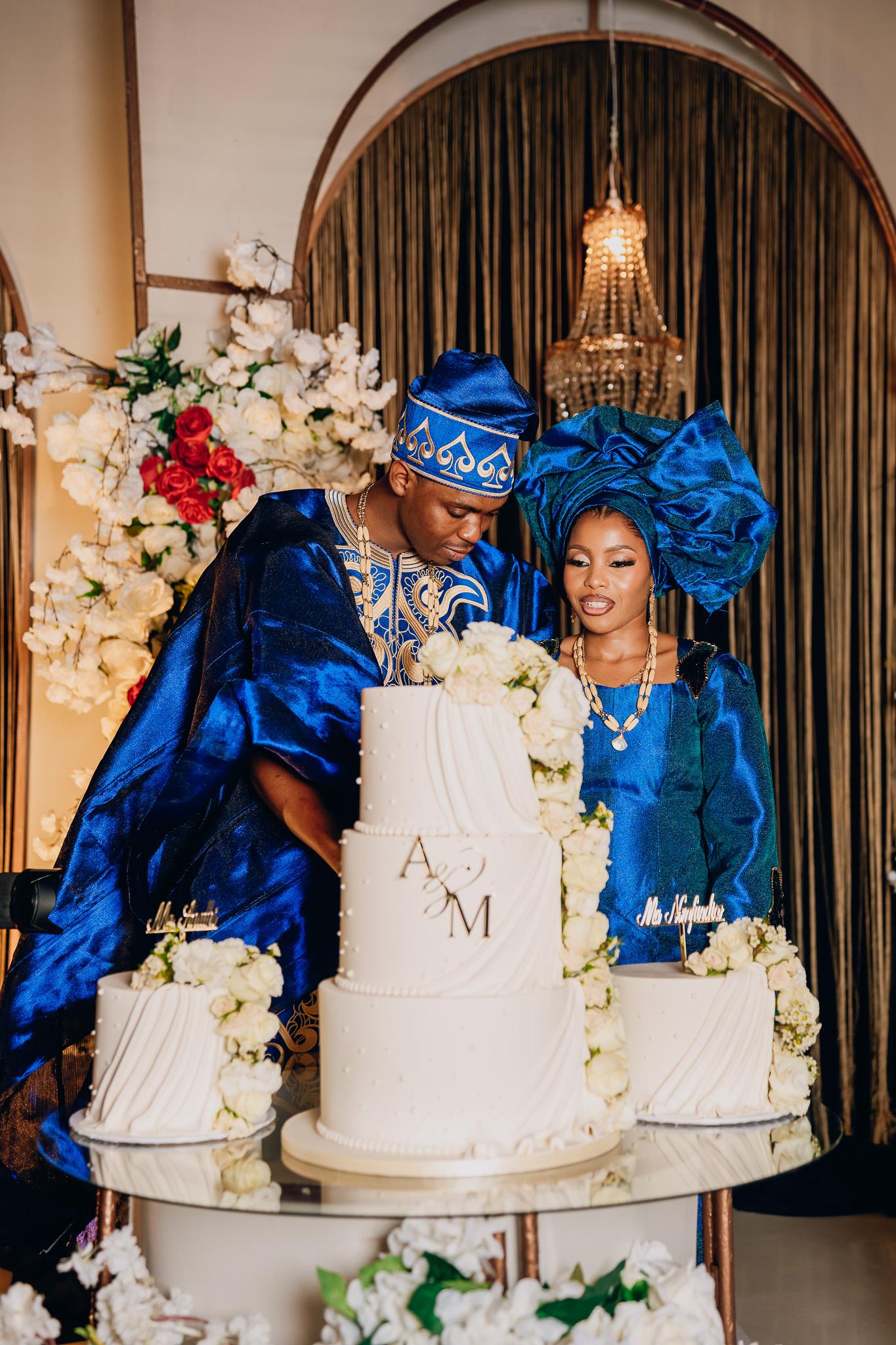 Couple in blue traditional attire beside their wedding cake.