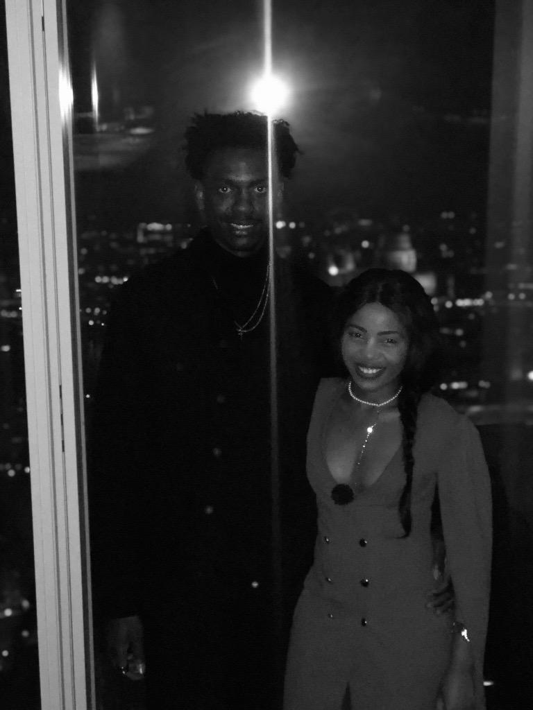 Afifoluwa and Mihlali dressed up beside the same window, the London skyline glowing behind them, in black and white